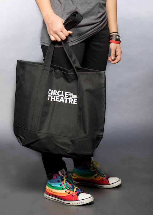 Black circle theatre tote held by woman wearing rainbow painted Converse.