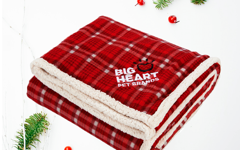 Promotional red plaid sherpa blanket with holly and berries in the background