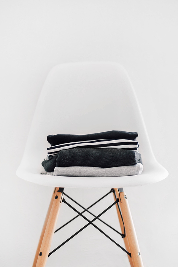 White chair with wooden legs, and shirts stacked on top.