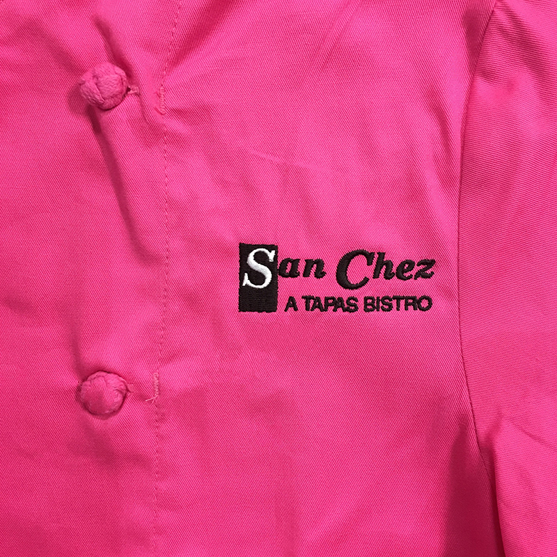 Black and white San Chez A Tapas Bistro embroidered on a bright pink chef's coat. Embroidered at MarkIt Merchandise.